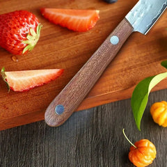 Wooden-handled knife on a wooden cutting board with sliced strawberries