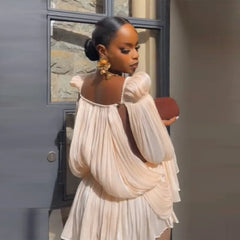 Woman in a beige dress holding a red clutch against a neutral background