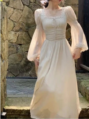 Woman wearing a white dress with sheer sleeves in front of a stone wall.