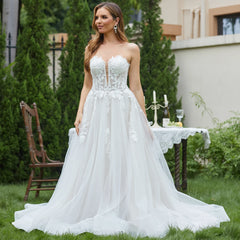 Woman in a white wedding dress standing outdoors with greenery and a table in the background