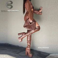 A woman wearing chocolate brown, thigh-high, platform high-heeled boots with a zipper closure. The boots have a block heel design and are above the knee.