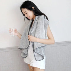 Woman holding a glass of water with a gray towel draped over her shoulders against a light background