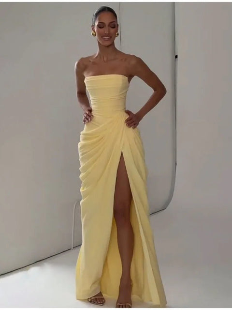 Woman wearing a yellow strapless gown with a high slit on a plain background