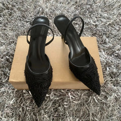 Black high-heeled shoes with embellishments on a cardboard box against a textured gray background