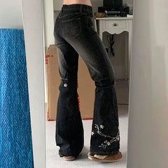 Person wearing black flared jeans with floral embroidery in a room.