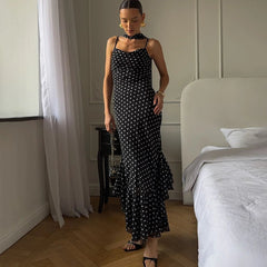 Woman in a black polka dot dress standing in a bedroom.