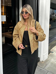 Woman wearing a gold jacket and black pants standing outside a building.