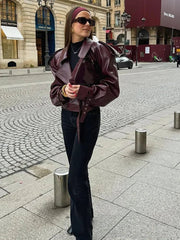 Woman in a burgundy leather jacket and black pants standing on a city street.