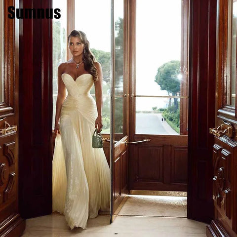Woman in a white evening gown standing in a doorway with a scenic view outside.