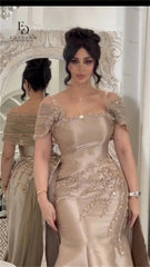 Woman in a beige evening gown with intricate detailing standing in front of a decorative mirror.