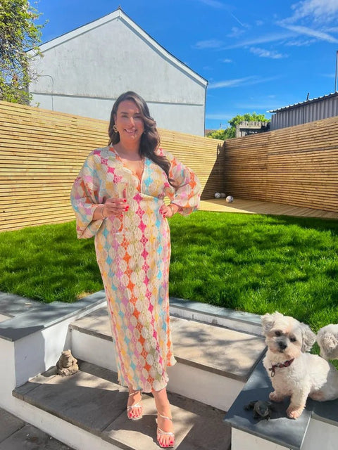 Woman in a colorful dress standing with a small white dog on a patio.