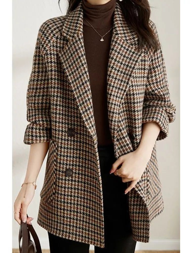 A woman wearing a checkered wool blazer with a notched collar and double-breasted closure, paired with a brown sweater and black trousers.