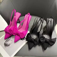 Pair of pink high-heeled shoes with bow detail on a gray surface