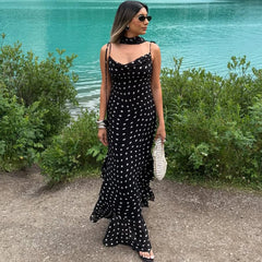 Woman in a black polka dot dress standing by a body of water.
