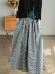 Person wearing a black jacket and a long, checkered skirt in a room with a wooden dresser.