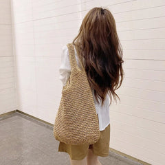 Person wearing a woven beige bag against a white wall
