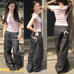 Woman wearing a pink shirt and black wide-leg jeans with heart designs, posing on steps.