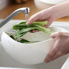 Person washing green leafy vegetables in a white colander under running water from a faucet.