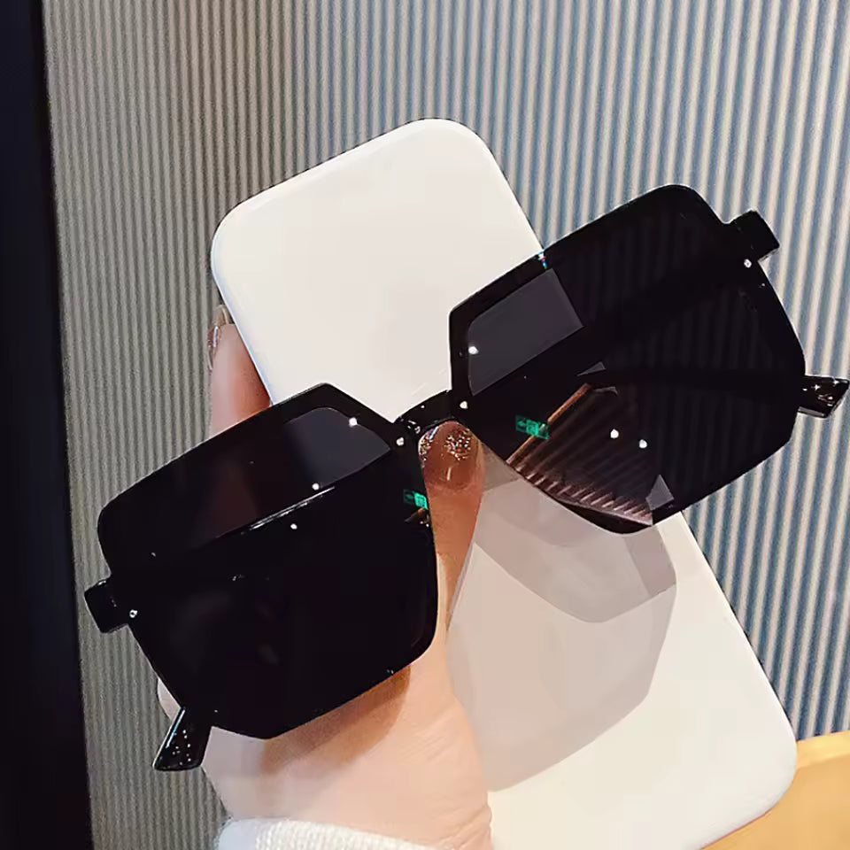 Black sunglasses held by a hand against a neutral background