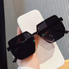 Black sunglasses held by a hand against a neutral background