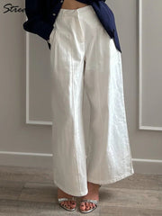 Person wearing white wide-leg pants with a navy jacket in a minimal indoor setting