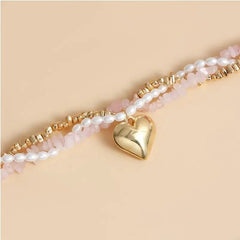 Bracelet with pearl beads and gold heart charm on a beige background