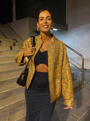Woman in a gold sequin jacket and black dress standing on steps.