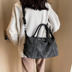 Person wearing a black handbag over one shoulder against a beige background