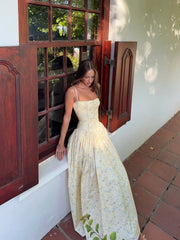 Woman in a floral dress standing near a window with wooden shutters.