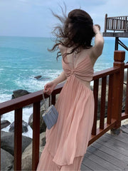 Woman in a pink dress standing on a wooden deck overlooking the ocean.