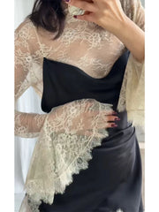 Person wearing a black top and black skirt with a beige lace shawl over shoulders.