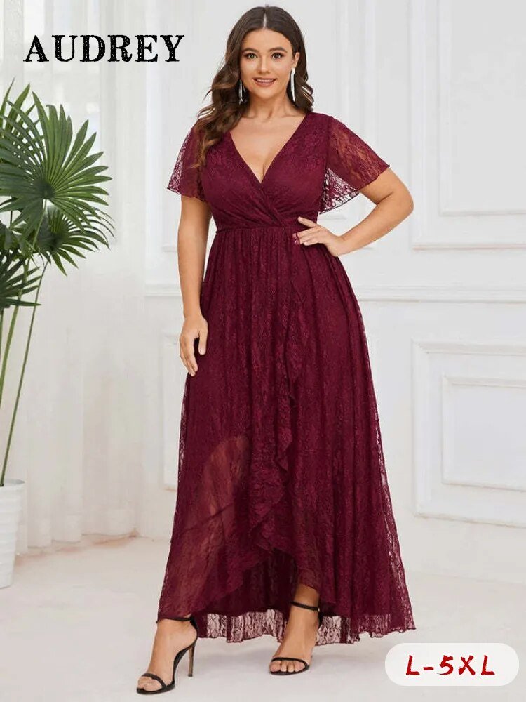 A woman wearing an elegant plus size lace dress with a V-neck, short ruffled sleeves, and an asymmetrical hemline in a dark burgundy color. The dress appears to be for formal occasions such as evening parties or weddings.