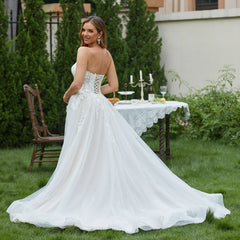 Woman in a white wedding dress standing outdoors with a table and chairs in the background.
