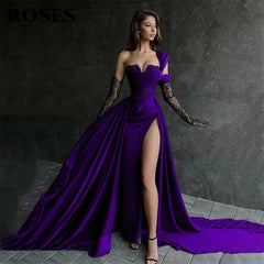 Woman in a long purple dress with a high slit standing against a dark background.