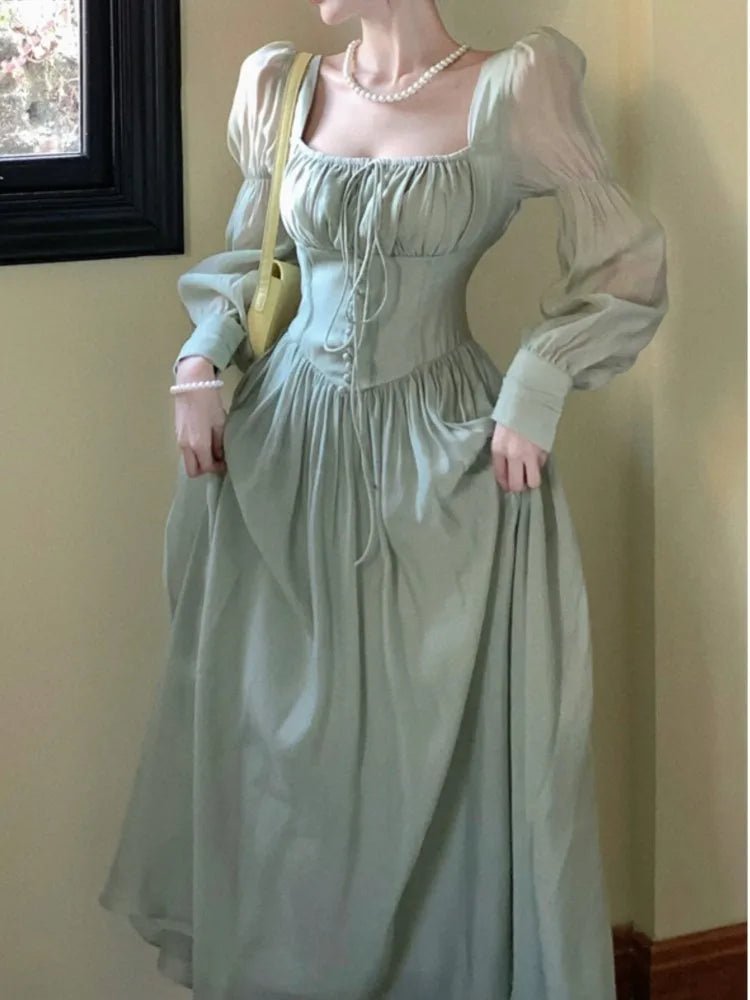 Person wearing a light green historical dress against a plain wall.