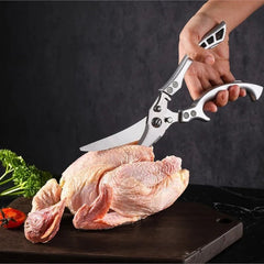 Person using poultry shears on a raw chicken on a dark surface with vegetables.