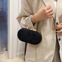 Person holding a black glittery clutch bag with a gold chain strap.
