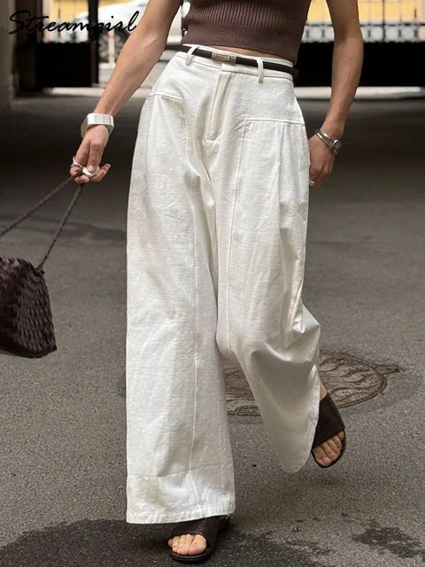 Person wearing white wide-leg pants and a brown top on a street.
