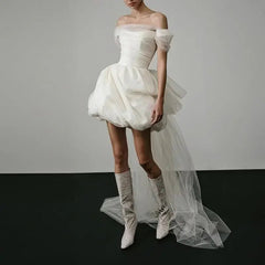White off-shoulder dress with a tulle skirt worn by a model on a plain background