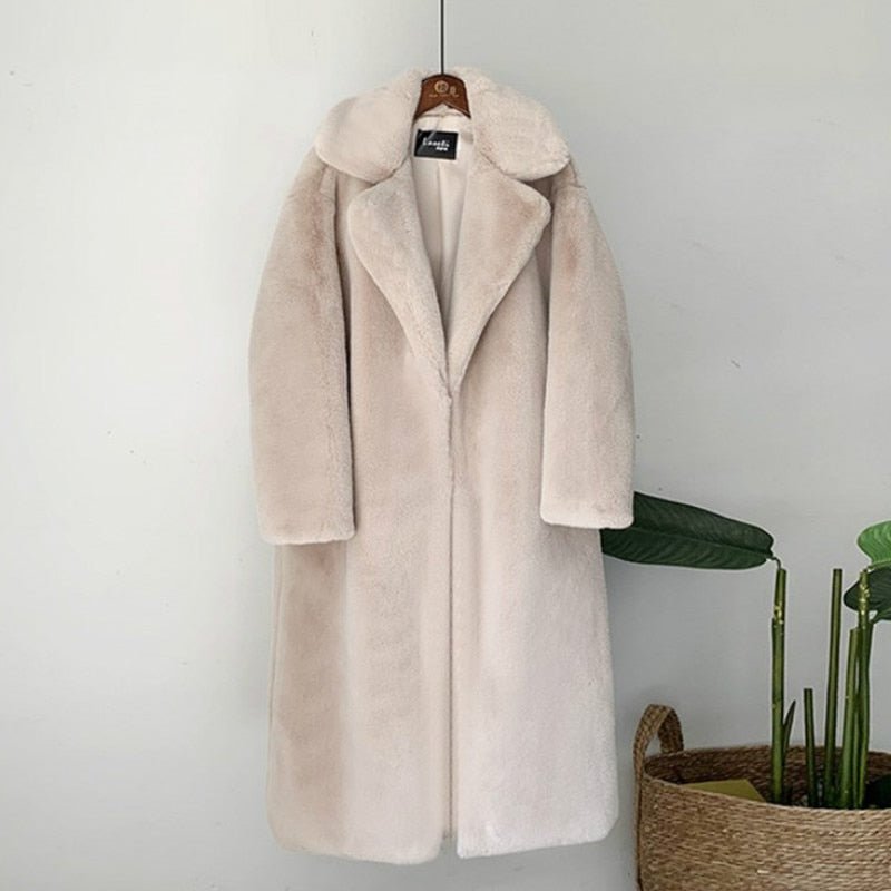 A long, white faux fur coat with a turn-down collar, displayed on a hanger against a neutral background with a plant in the foreground.