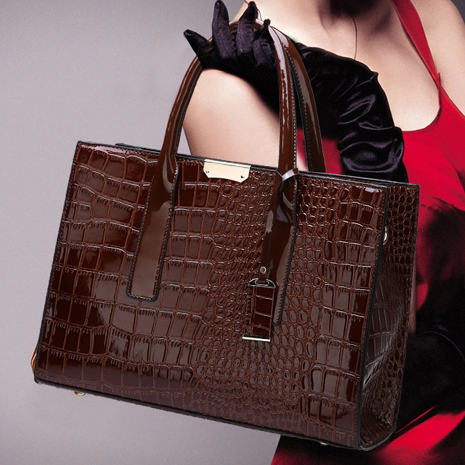 A brown crocodile embossed vegan leather tote bag with a large capacity, held by a woman in a red dress. The bag has comfort-grip handles and a zipper closure.