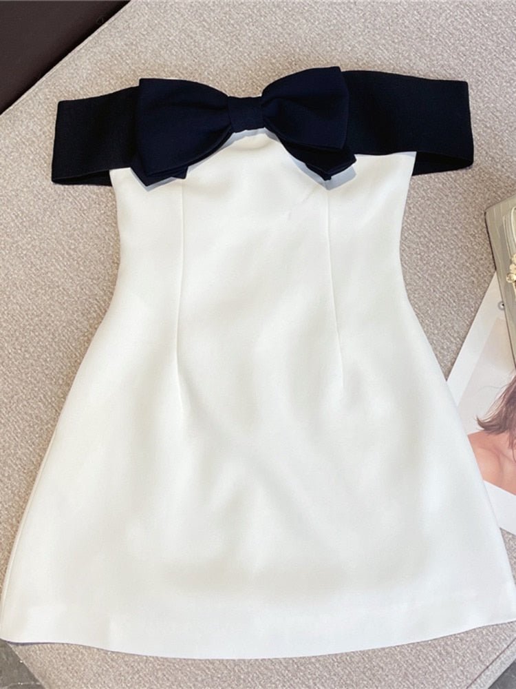 A sleeveless black and white mini dress with a bow decoration, displayed on a flat surface.