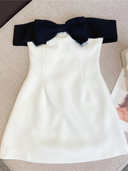 A sleeveless black and white mini dress with a bow decoration, displayed on a flat surface.