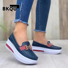 A pair of navy blue platform loafers with red accents and a metal buckle, worn by a woman with jeans.