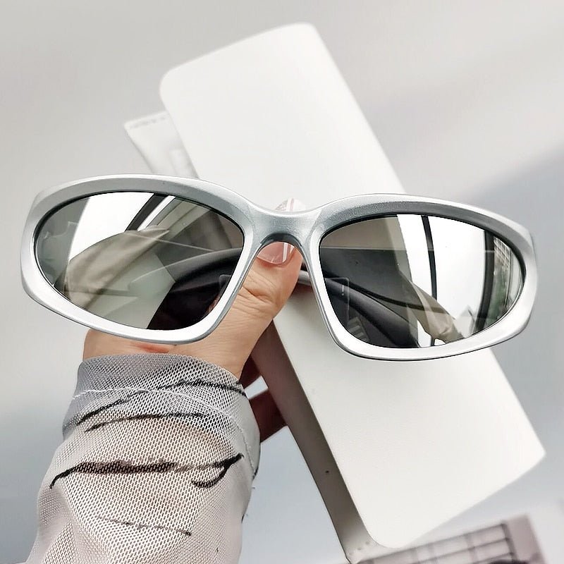 A pair of silver oval-shaped sunglasses with a mirrored finish, displayed on a hand against a neutral background.