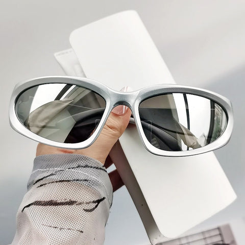 A pair of silver oval-shaped sunglasses with a mirrored finish, displayed on a hand against a neutral background.