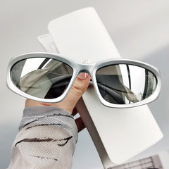 A pair of silver oval-shaped sunglasses with a mirrored finish, displayed on a hand against a neutral background.