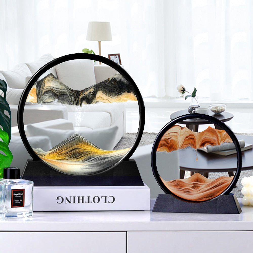 A round moving sand art piece with a black outer frame and a transparent glass panel, showing colored sand creating mountain-like formations inside.