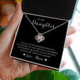 A necklace with a silver or gold colored pendant in the shape of a love knot, displayed in a black box with a message card.