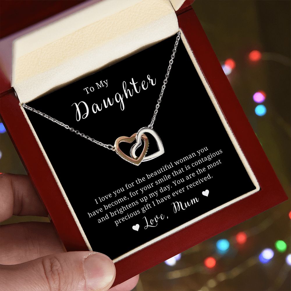 A necklace with two heart-shaped pendants, presented in a box with a Christmas tree decoration in the background.